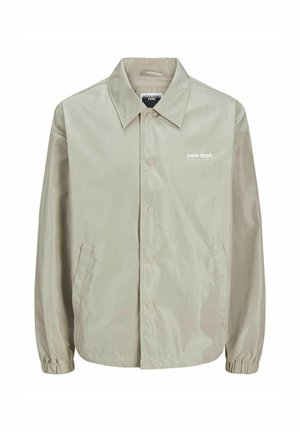 Gaiši bež žakete, kas izgatavota no gludas, vieglas auduma. Aprīkota ar apkakli, priekšējiem pogām, sānu kabatām un ribotiem piedurknēm. Izdrukāts logo uz krūtīm.