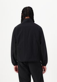 Chaqueta ligera negra con cuello alzado, puños elásticos y un corte relajado. Fabricada en tejido texturizado, con un diseño suave y simple.