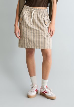 Karierter beiger Rock mit elastischem Bund und Kordelzug, ausgestattet mit Seitentaschen und geradem Schnitt, kombiniert mit weißen Turnschuhen.