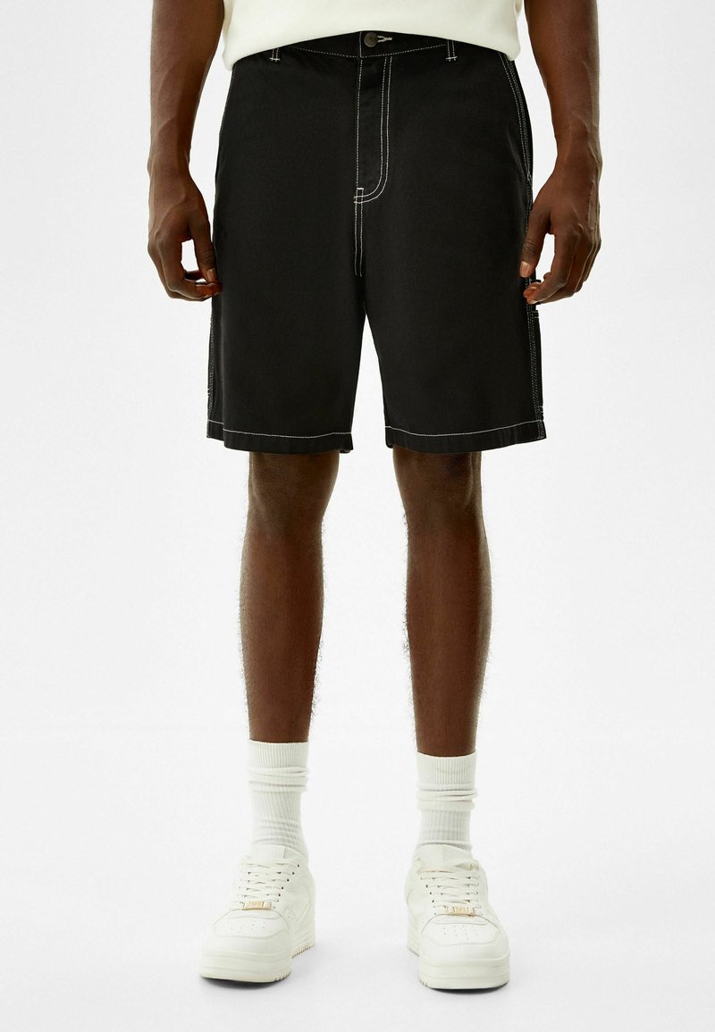 Mustat farkkushortsit, joissa on valkoiset ompeleet, rento malli ja sivutaskut. Yhdistetty valkoisten tennareiden ja lyhyiden sukkien kanssa.