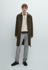 Brown wool coat with a button front, grey knit polo with three buttons, grey denim pants, and black shoes. Solid color, minimal design.