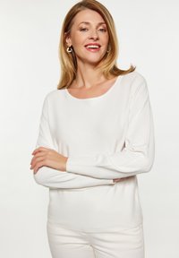 Cămașă albă cu mânecă lungă dintr-un material ușor și moale, cu o ușoară strălucire, având un guler rotund și manșete cu nervuri.