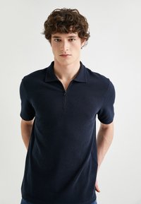 Marinblå kortärmad polotröja med strukturerad tyg, dragkedja i kragen och en figurnära design. Lämplig för avslappnad användning.