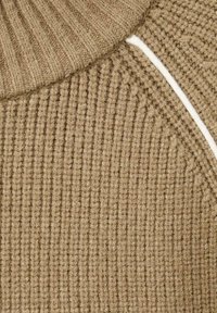 Suéter beige de punto con textura acanalada, cuello alto y detalles en blanco. La tela parece suave y cómoda.