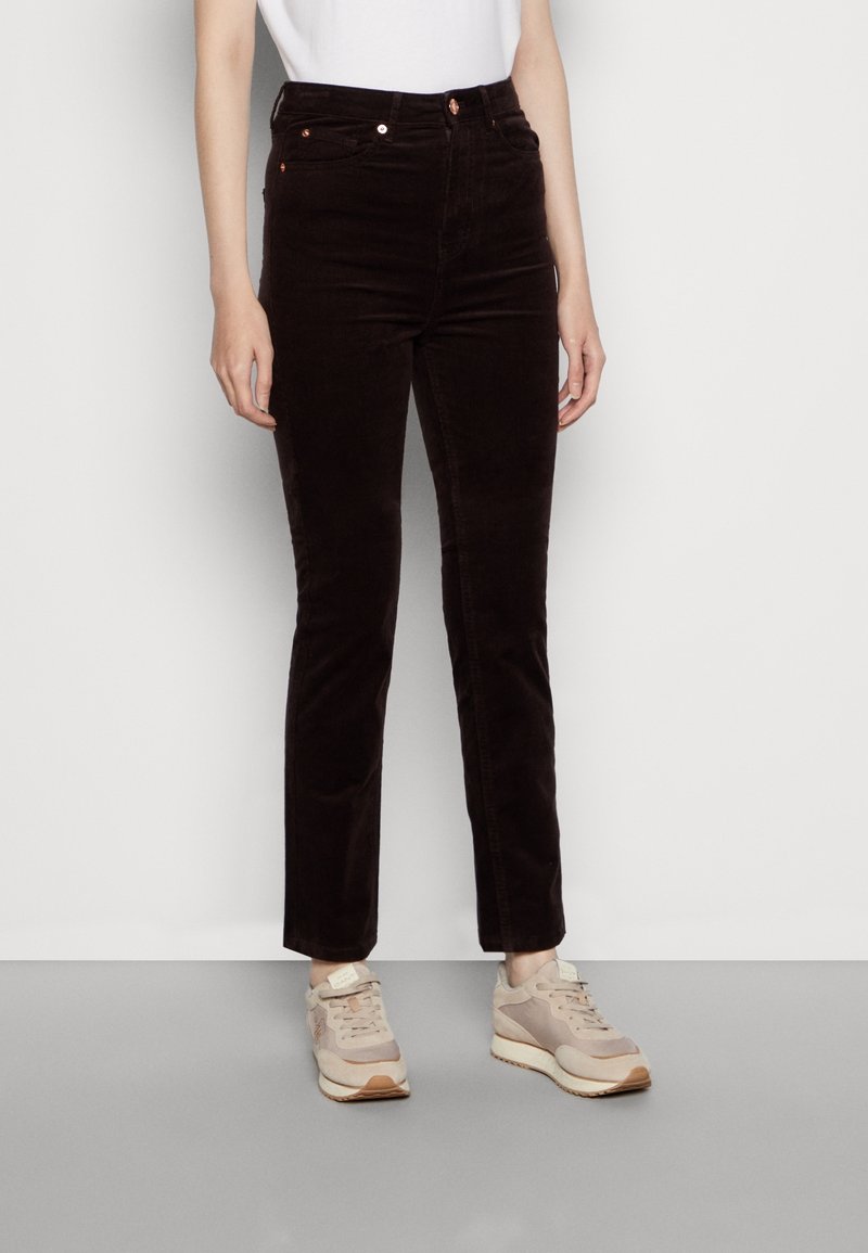 Pantalons en velours côtelé marron avec une coupe ajustée, dotés de poches avant et de coutures discrètes. Portés avec des baskets de couleur claire.