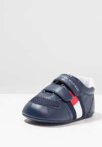 Námornické modré dětské boty vyrobené z kůže, s suchým zipem, bílými a červenými pruhy a zaoblenou špičkou.