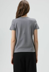 Grijs T-shirt met korte mouwen en een ronde hals, met een gladde textuur en zichtbare stikdetails, gedragen met een zwarte broek.