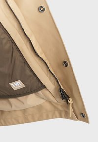 Beige Regenjacke mit Innenfutter in kontrastierendem Braun. Verfügt über einen Reißverschluss und einen Druckknopfverschluss; sichtbares Markenetikett auf dem Futter.