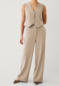 Beżowa, dopasowana kamizelka z dekoltem w serek, zapinana na cztery guziki, zestawiona ze spodniami o szerokich nogawkach. Tkanina o fakturze z gładkim wykończeniem. Buty na obcasie z motywem zwierzęcym.