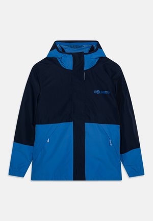 Blue and navy windbreaker jacket with hood, featuring zippered pockets and elastic cuffs. Logo on the chest area, lightweight fabric.