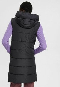 Czarna kamizelka puchowa z kapturem, pikowanym wzorem i długim krojem. Rękawy wykonane z prążkowanego dziania w jasnym fioletowym kolorze. Charakteryzuje się gładką fakturą i wykończeniem.