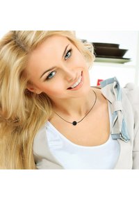 Collier de perles noires sur un mince cordon noir porté avec un chemisier beige présentant un détail de col rayé. Les cheveux sont longs et blonds.