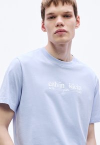 Svetlomodré bavlnené tričko s okrúhlym výstrihom, krátkymi rukávmi a bielym nápisom "calvin klein new york city" na hrudi.