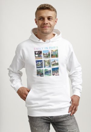 Młody mężczyzna noszący białą bluzę z kapturem z dziewięcioma kolorowymi zdjęciami tematycznie związanymi z Paryżem oraz napisem „EMILY IN PARIS” przez środek klatki piersiowej.