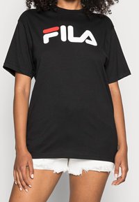 T-shirt en coton noir à manches courtes, avec un logo FILA blanc et rouge bien en vue sur la poitrine. Design classique à col rond.
