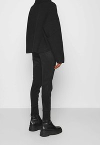 Svart stickad tröja med hög krage, boxig passform och ribbat mönster, i kombination med svarta slim fit-byxor och kraftiga svarta stövlar.