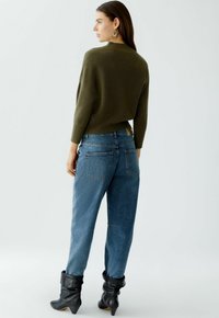 Olivgrüner gerippter Pullover kombiniert mit lockeren blauen Denim-Jeans, die über Taschen auf der Rückseite verfügen, und schwarzen lässigen Stiefeletten. Einfacher, lässiger Look.