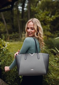 Graue Tragetasche aus strukturiertem Material mit zwei stabilen Griffen, versehen mit einem V-förmigen Akzent und einem Logo auf der Vorderseite.