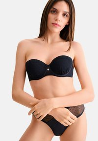 Soutien-gorge noir sans bretelles en tissu texturé, avec des accents décoratifs et un slip à pois assorti. Matériau lisse et design ajusté.