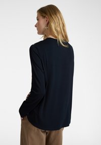 Marineblaues Langarmoberteil mit rundem Halsausschnitt, gemusterten Ärmeln, weichem Material und lockerer Passform. Subtile Textur und fließender Schnitt.