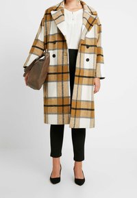 Wool plaid coat in yellow, white, and gray with a relaxed fit, large collar, and two front buttons, paired with black pants and a brown bag.