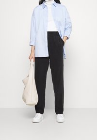 Lichtblauw overhemd met knopen, witte coltrui, zwarte broek, witte sneakers en een gestructureerde beige draagtas. Eenvoudig ontwerp en casual pasvorm.