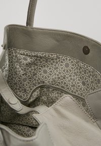 Szara skórzana torba tote z dekoracyjną wewnętrzną podszewką z geometrycznym wzorem w jasnych odcieniach. Zawiera dwa uchwyty i zapięcie na zatrzask.