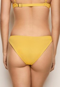 Gul bikiniunderdel med texturerat hexagonmönster. Låg midja ger en söt täckning. Slät tyg utan synlig hårdvara eller detaljer.