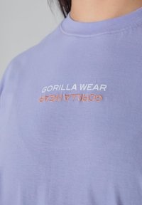 Lilac short-sleeve t-shirt with a crew neck, featuring "GORILLA WEAR" in white and orange text. Smooth cotton material with minimal texture.