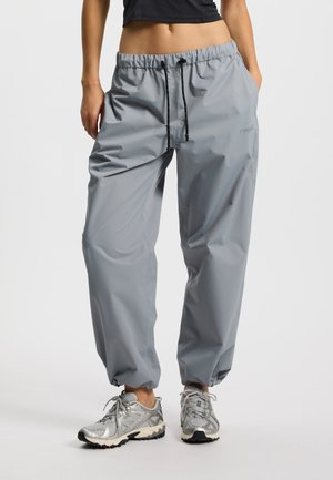 Lekkie szare spodnie przeciwdeszczowe z elastycznym pasem, regulowanym sznurkiem i elastycznymi mankietami; wykonane z materiału wodoodpornego.