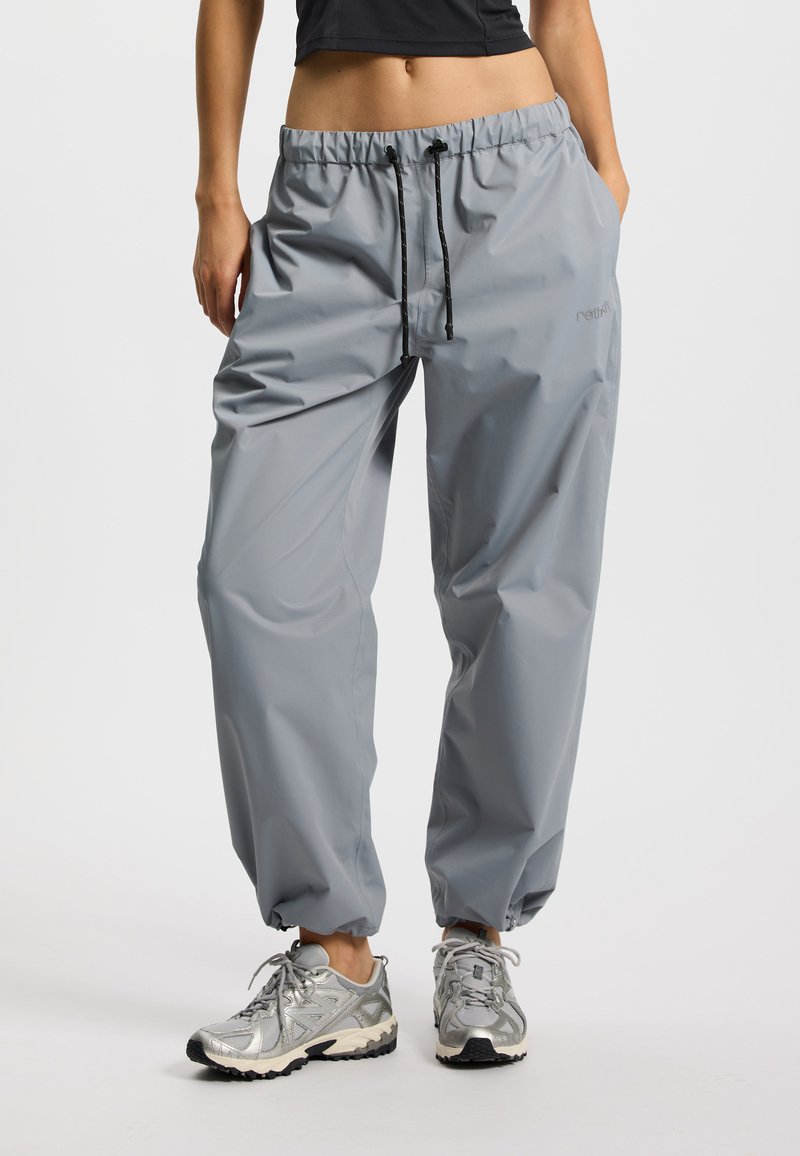 Lekkie szare spodnie przeciwdeszczowe z elastycznym pasem, regulowanym sznurkiem i elastycznymi mankietami; wykonane z materiału wodoodpornego.