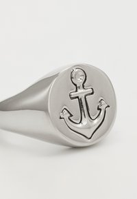 Sølvanker ring med en avrundet overflate, som har et polert anker-design. Jevn tekstur og litt buet ring.