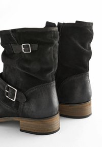 Décolleté in suede nero con punta tonda, dettagli in fibbia argentata e tacco in legno con finitura testurizzata. Chiusura con cerniera laterale.