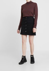 Dlouhý pruhovaný top v barvě bordó a námořnické modři, doplněný černou džínovou sukní s předními knoflíky a černými kotníkovými botami.