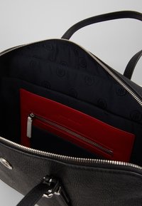 Bolso de mano de cuero negro con cierre de cremallera. El interior presenta un forro de tela oscura y un compartimento rojo con cremallera. Cuenta con dos asas.