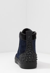 Granatowe zamszowe botki sięgające do kostek z teksturowaną czarną gumową podeszwą i kolcami na obcasie, z zamkiem błyskawicznym i wyściełanym kołnierzem wokół kostki.