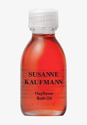 Orangenbadöl in einer transparenten Glasflasche mit einem weißen Schraubverschluss. Schwarzer Text lautet "SUSANNE KAUFMANN Heu-Flower-Badöl."