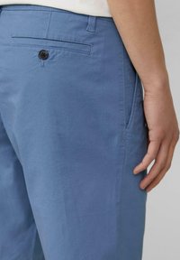 Lichtblauwe broek van katoen, met een achterzak die sluit met een zwarte knop en zichtbare stikdetails.