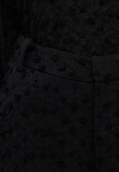 Black textured fabric featuring a raised pattern, with a smooth waistband detail. The overall design is sleek and minimalist.