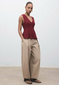 Burgundy peplum-top med djup V-ringning, parat med beige vida byxor. Slät tyg med en strukturerad siluett och avslappnad passform.