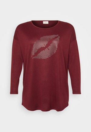 Burgundská dlhá rukávová blúzka z mäkkej tkaniny s potlačou pier na strednej časti pokrytou striebornými nitmi. Okrúhly výstrih a mierne zaoblený okraj.