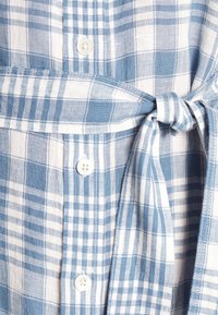 Modré a bílé kostkované látky s bílými knoflíky a uvázaným páskem na pase, naznačující oděv, jako je šaty nebo košile.