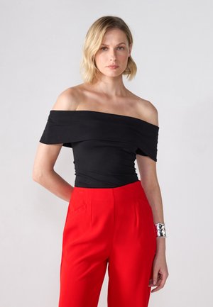 Top nero senza spalle con design aderente, abbinato a pantaloni rossi a vita alta. Bracciale a manica in metallo argentato al polso. Tessuto di texture liscia.