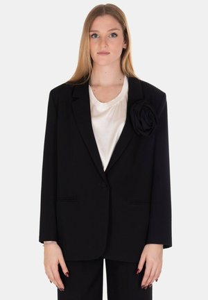 Blazer nero con un design strutturato, caratterizzato da una grande accentuazione di rosa in tessuto sul risvolto sinistro. Texture liscia e chiusura con un solo bottone.