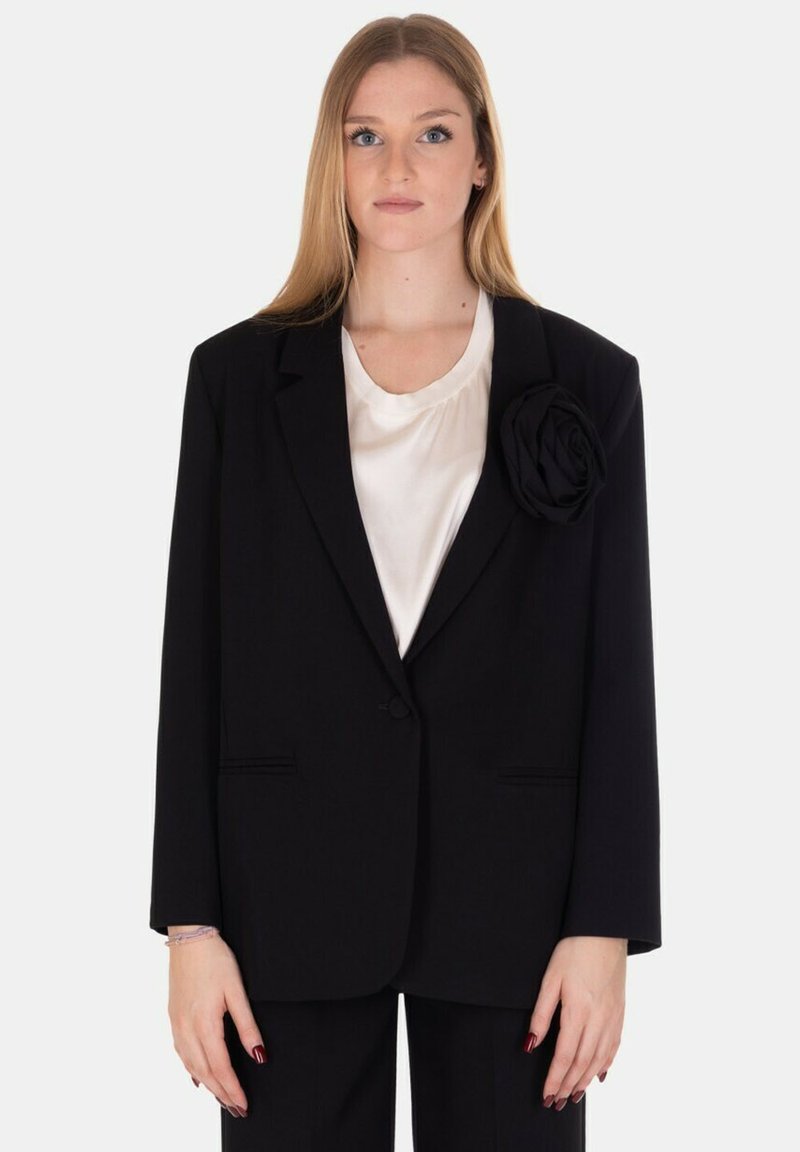 Blazer nero con un design strutturato, caratterizzato da una grande accentuazione di rosa in tessuto sul risvolto sinistro. Texture liscia e chiusura con un solo bottone.