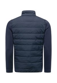 Laivastonsininen toppatakki, jossa on tikattu etuosa ja yksiväriset hihat, korkea kaulus ja joustavat hihansuut istuvan näköistä varten.