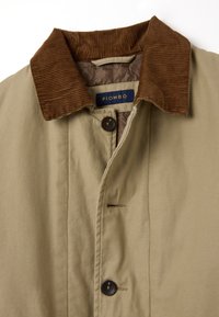 Giacca beige con colletto in velluto a coste marrone, caratterizzata da una chiusura a bottoni e dettagli di cucitura discreti. Etichetta visibile all'interno con "PIOMBO."