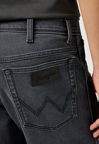 Jeans in denim scuro con una patch in pelle nera e cuciture a contrasto; presentano tasche posteriori angolate con un design distintivo a forma di W.