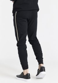 Svarta joggerbyxor med en slim fit, med vita sidostripes. Kombinerade med svarta lädersneakers och en texturerad midja.