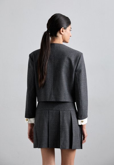 Grijze tweed blazer met een cropped ontwerp, voorzien van lange mouwen en witte manchetten. Gecombineerd met een geplooide grijze miniskirt.